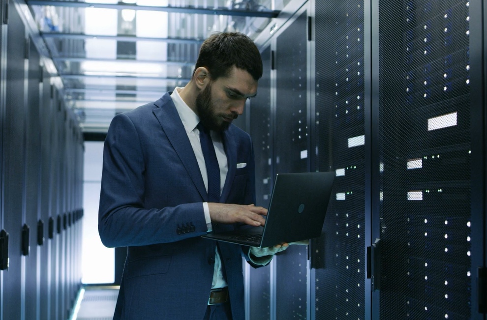 Professional man in suit standing in a server room filled with computer servers and network equipment for Transition of IT Systems in Mergers & Acquisitions