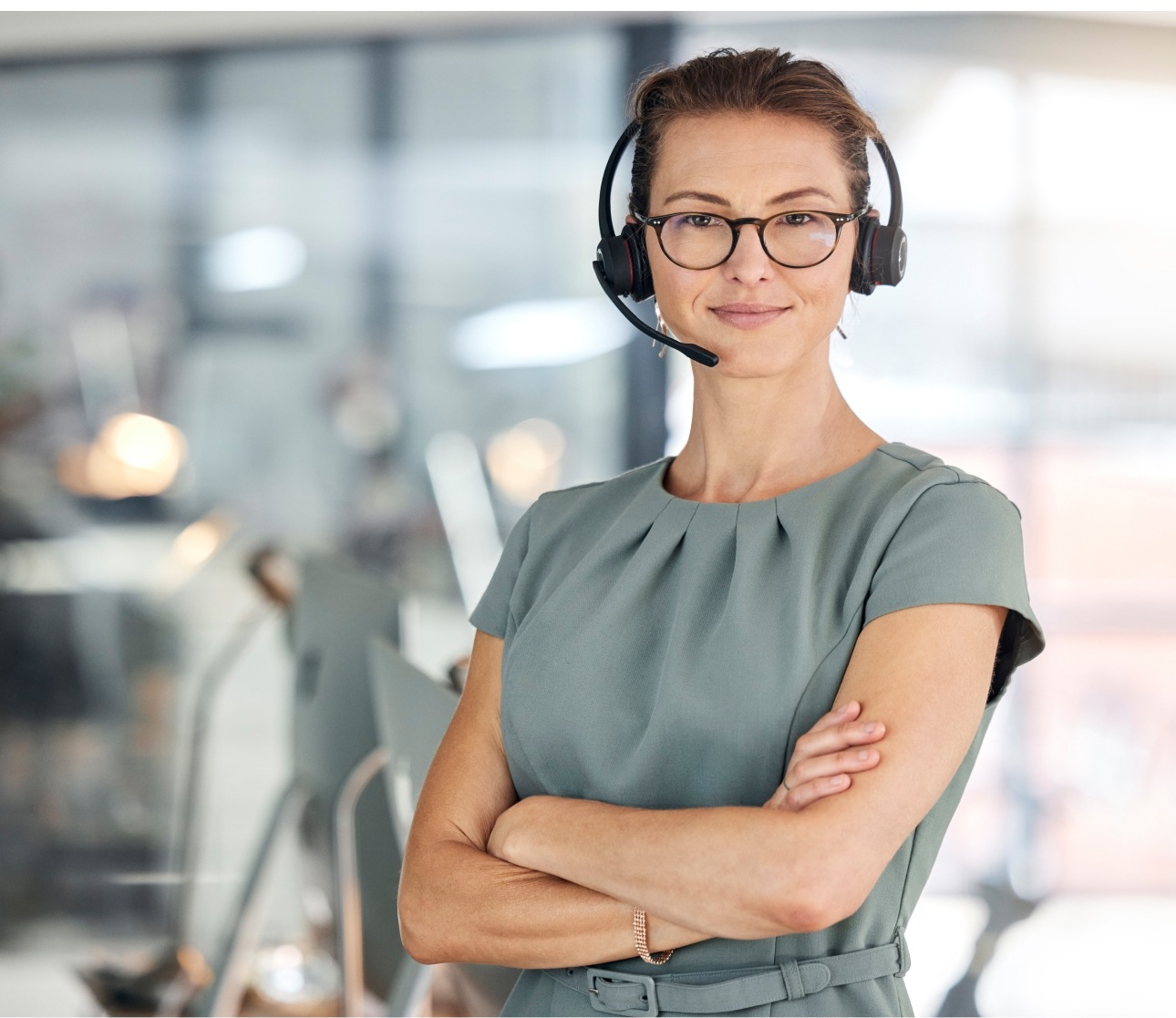 A woman wearing a headset and glasses stands in front of a desk, ready to assist with customer service or technical support.